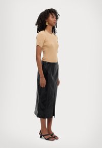 Beige ribbes t-skjorte med kort erme og knapper, kombinert med en svart teksturert knelang skjørt og svarte sandaler med åpen tå.