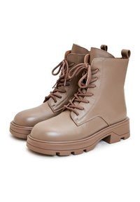 Botas de cuero marrón hasta el tobillo con suelas gruesas, punteras redondeadas y diseño de cordones. Cuenta con una pestaña en la parte posterior para un fácil calzado.