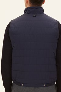 Marinblå puffväst med horisontellt quiltat mönster, hög krage och tryckknappsförslutning nederst. Materialet verkar slätt och isolerat.