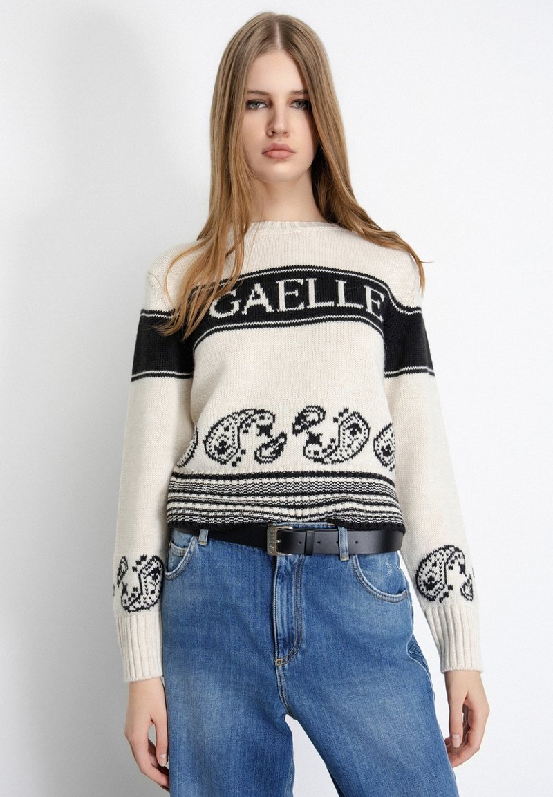 Maglione lavorato a maglia di colore crema con accenti neri e un intricato motivo paisley, con una fascia con logo, abbinato a jeans blu a vita alta.