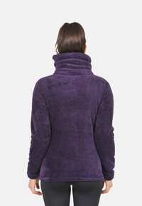 Pull violet en polaire avec un col haut, des manches longues et un tissu doux et texturé. Conçu pour la chaleur et le confort par temps frais.