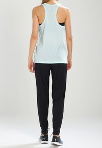 Ljust blå ärmlös tanktop med racerback-design, kombinerad med svarta joggerbyxor. Både plagg har mjuka texturer och avslappnad passform.