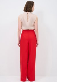 Beige mouwloze blouse met een keyhole-detail op de rug, gecombineerd met hoge, wijdvallende rode trousers, gladde stof, op maat gemaakt pasvorm.