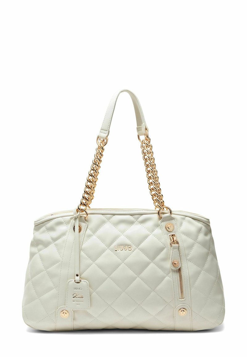 Sac en crème matelassé avec poignées en chaîne dorée, poche zippée et détail du logo sur une texture semblable au cuir.