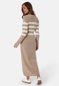 Abito lavorato a maglia beige con strisce orizzontali bianche, caratterizzato da un busto aderente e maniche lunghe, che si estende fino alla caviglia, abbinato a sneakers bianche.