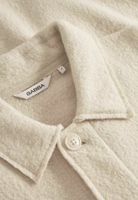 Světle béžová košile z vlněné směsi s límečkem, jedním bílým knoflíkem a štítkem GABBA ve výstřihu. Měkčená, strukturovaná tkanina.