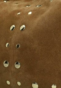 Bruin suède materiaal met een zachte textuur, voorzien van metalen zilveren studs in een gevarieerd patroon over het oppervlak.
