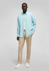 Lichtblauw overhemd van linnen, gecombineerd met beige linnen broek en witte sneakers. Het overhemd heeft een relaxte pasvorm en lange mouwen.