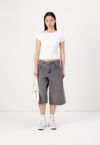 Hvit tettsittende kortermet topp kombinert med grå denim culottes. Modellen holder en liten hvit håndveske og har på seg hvite høye sneakers.