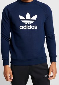 Námořnicky modrá mikina Adidas s bílým logem trefoil, žebrovaným kulatým výstřihem a manžetami; vyrobená z měkké, strukturované bavlněné směsi.