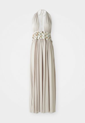 Maxi dress in light beige fabric, featuring a halter neck, gathered skirt, and decorative metallic coin accents at the waist.