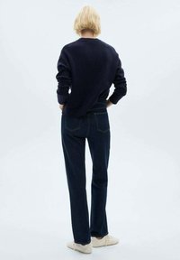 Pulover navy cu o croială lejeră și mansete cu țesătură în relief, asortat cu blugi straight-leg bleu închis. Încălțăminte în nuanțe neutre completează ținuta.
