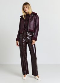 Veste de biker en cuir bordeaux avec un col texturé, associée à un pantalon large en cuir brun brillant et des chaussures à talons hauts crème.