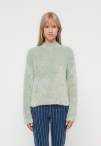 Flauschiger, hellgrüner Pullover mit hohem Kragen und langen Ärmeln. Die Textur ist weich und hat ein leicht gekürztes Design.