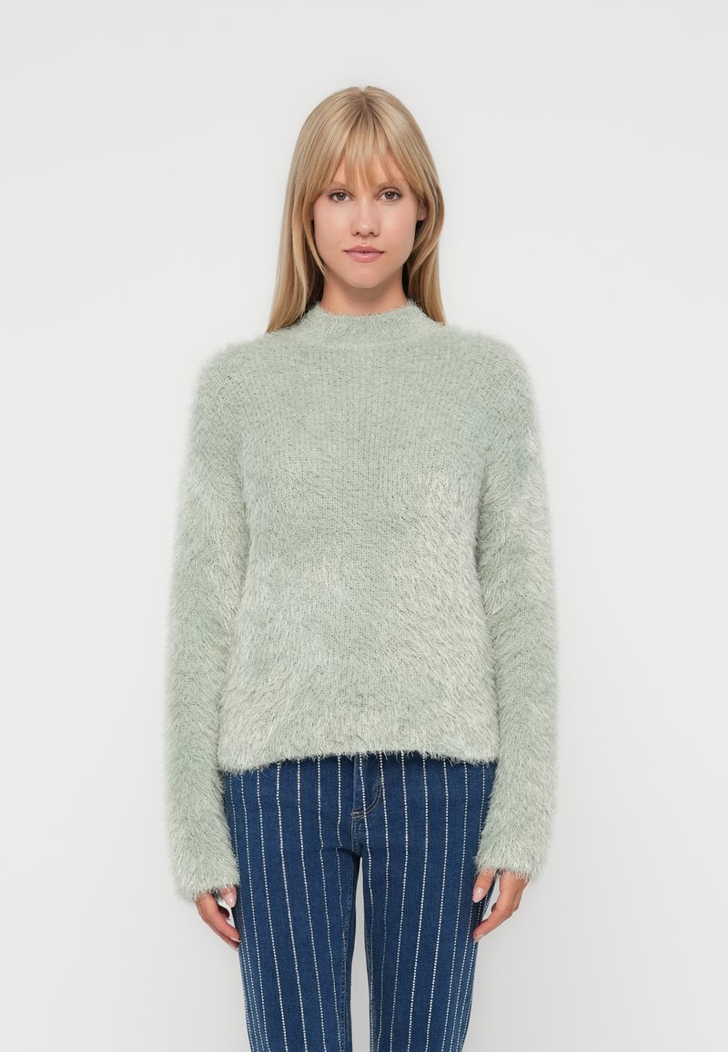 Flauschiger, hellgrüner Pullover mit hohem Kragen und langen Ärmeln. Die Textur ist weich und hat ein leicht gekürztes Design.