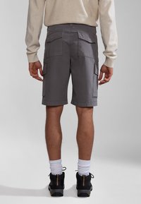 Pantaloni cargo grigi con molteplici tasche, realizzati in tessuto leggero. Presentano orli arrotolati e una vestibilità comoda, abbinati a scarpe nere e calzini bianchi.