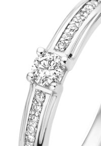 Bague en diamant avec une pierre centrale ronde, montée sur une bande en argent poli. Huit petits diamants bordent le côté de la bande, ajoutant de l'éclat.