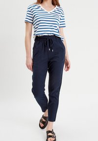 Randig blå och vit V-ringad t-shirt i kombination med marinblå byxor med dragsko. Texturerad tyg, avslappnad passform och svarta sandaler fulländar looken.