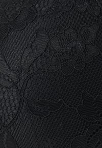 Tissu noir avec un design en dentelle florale, présentant des motifs en relief et un arrière-plan texturé. Motifs floraux sombres et complexes tout au long.