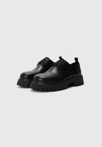 Chaussures noires en cuir à lacets avec un bout arrondi, semelle en caoutchouc texturé et design épais. Présente un petit talon et une languette.