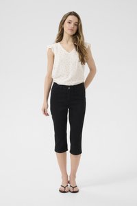 Pantaloni capri neri slim fit, abbinati a una blusa crema con pois neri e maniche a volant, e infradito nere.