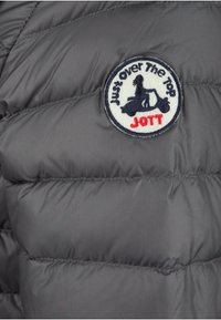 Grijze gewatteerde jacksectie met een rond stoffen logo met een scooterafbeelding en de tekst "Just Over The Top JOTT" in blauw en rood.