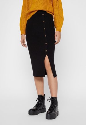 Czarna midi spódnica z przednim rozcięciem i detalami z guzikami, zestawiona z teksturowanym, musztardowym swetrem oraz masywnymi czarnymi botkami na sznurowadła.