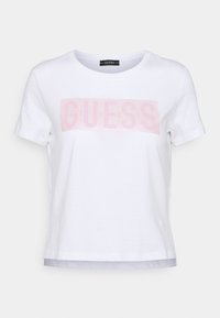Bílý bavlněný tričko s světle růžovým logem "GUESS" přes hrudník, krátké rukávy a kulatým výstřihem s kontrastním lemem.