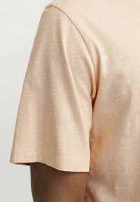 Short-sleeve beige t-shirt, made of lightweight, textured fabric. Features a relaxed fit and subtle stitching along the hem and sleeve.