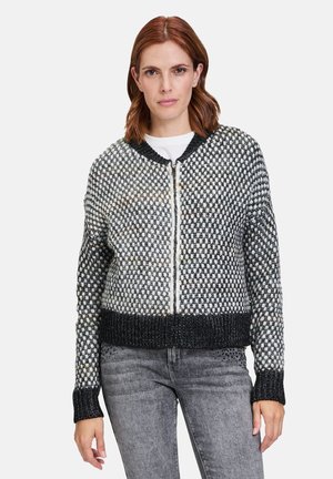 Cardigan en tricot noir et blanc, présentant un motif texturé, des poignets et un ourlet côtelés, avec une fermeture éclair à l'avant.