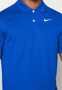 Polo blu realizzato in tessuto morbido con colletto classico, tre bottoni e logo Nike bianco sul lato sinistro del petto.