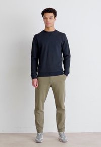 Czarna bluza z ribbowanymi mankietami i dołem, zestawiona z oliwkowymi spodniami i szarymi trampkami. Prosty design, luźny fason, minimalne logo.