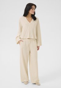 Krämfärgad loungewear-set bestående av en kortärmad, v-ringad långärmad topp och lösa, snörningbyxor i ett mjukt, texturerat tyg.