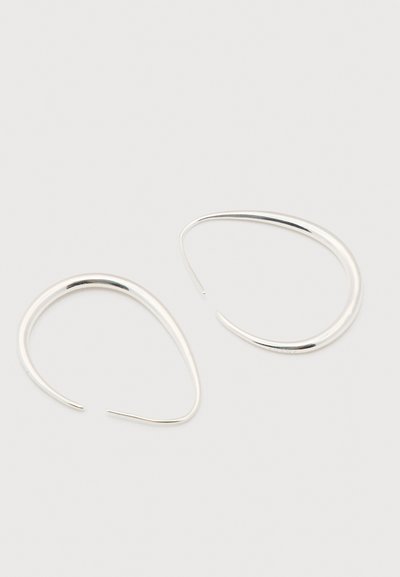 Para gładkich, srebrnych, łezkowatych kolczyków typu open hoop na jasnoszarym tle.