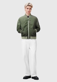 Olive green bomber jacket with ribbed cuffs and hem, zip closure, and a chest pocket, paired with white straight-leg pants and black shoes.