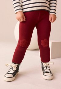 Burgundowe legginsy bawełniane z kwiatowymi łatami na kolanach, zestawione z czarnymi sneakersami za kostkę z białymi sznurówkami i kontrastującą podeszwą.