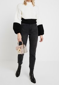 Maglione lavorato a maglia spesso con sezioni in bianco e nero, colletto alto, abbinato a jeans neri e stivaletti neri. Piccola borsa leggera con frange.