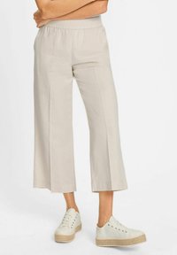 Beige cropped pants made of lightweight fabric with an elastic waistband, paired with white sneakers featuring a jute platform sole.