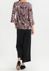 Blus i mauve med blomstertryck, flared ärmar och rynkig nederkant, tillsammans med svarta vida byxor och svarta slip-on skor.