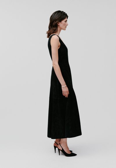 Zwarte mouwloze midi-jurk met een getailleerd lijfje en een uitlopende rok. Gemaakt van zachte, gestructureerde stof. Gecombineerd met zwarte slingback hakken.