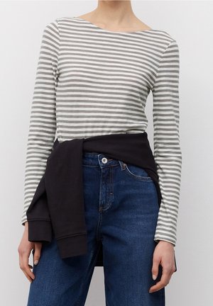 Top de manga larga a rayas en gris y blanco, con escote barco. Combinado con vaqueros de mezclilla azul oscuro y una sudadera negra atada a la cintura.