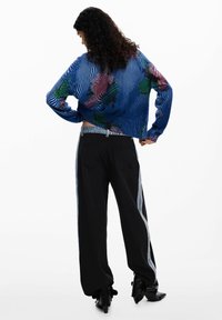 Blauer Strickpullover mit gestreiftem Muster und floralen Akzenten, kombiniert mit hoch taillierter schwarzer Hose mit seitlichem Streifendetail.