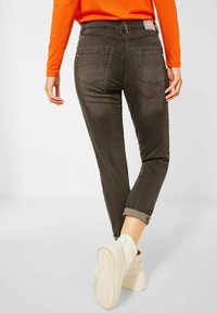 Tmavě hnědé kostkované elastické kalhoty s úzkým střihem, s manžetami na koncích a zadními kapsami. Kombinované se světlými kotníkovými botami.