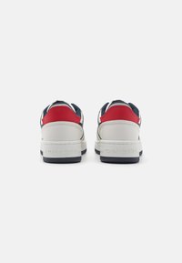 Zapatillas blancas con acentos en rojo y marino, fabricadas con materiales de cuero y textil, que cuentan con una suela gruesa y el logotipo en relieve "TOMMY JEANS" en el talón.