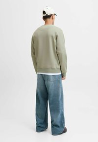 Lichtgroene sweatshirt met lange mouwen, ronde halslijn en geribde boorden, gecombineerd met losse blauwe jeans en een witte pet.