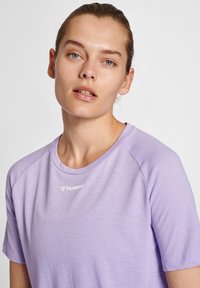 Ljust lila sport-t-shirt i texturerad tyg, med korta ärmar och rundad hals, samt en vit logotyp på bröstet.