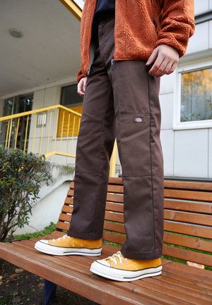 Brown pants with a straight cut, constructed from sturdy fabric, paired with bright yellow sneakers and an orange fleece jacket.
