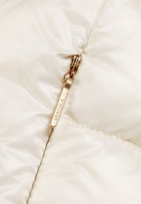 Beige pufferjacka med diagonalt ribbat mönster. Har en guldfärgad dragkedja med en märkesdragare som har texten "DUVETICA."