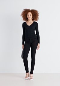 Top negru cu mâneci lungi și guler cu margini ondulate, asociat cu pantaloni negri strâmți și sandale cu toc argintii. Include o mică geantă neagră.
