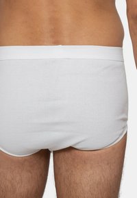 Slip bianchi a costine elasticizzate con una cintura morbida, che mostrano una vestibilità aderente e una texture liscia su gambe color carne.